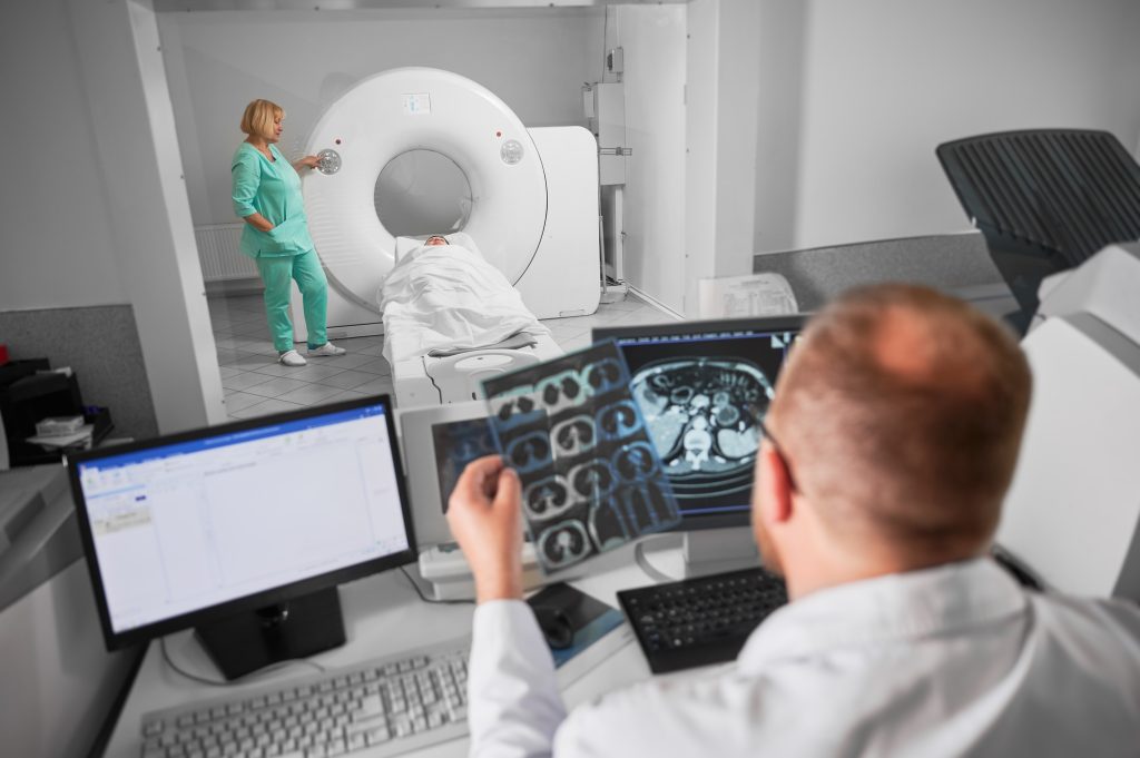 Male doctor sitting at computer, nurse making MRI.