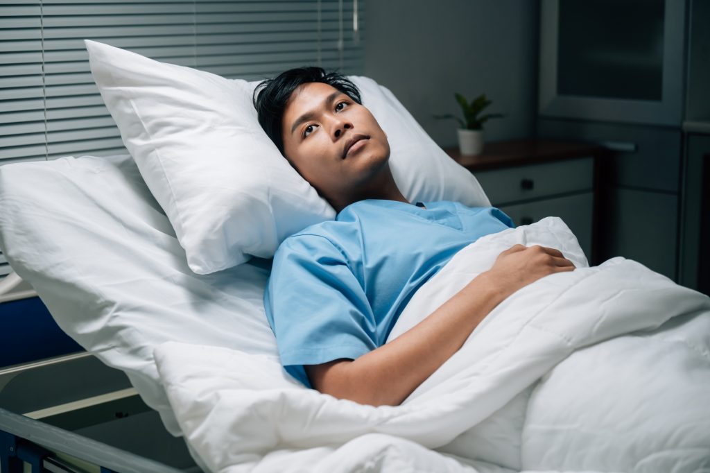 Young asian man lying in hospital bed is hoping for recovery after surgery